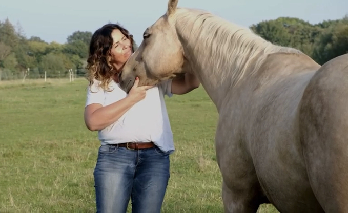 Tierkommunikatorin steht mit ihrem Pferd auf der Weide und hat seinen Kopf in voller Verbundenheit in der Hand und streichelt ihr Pferd.