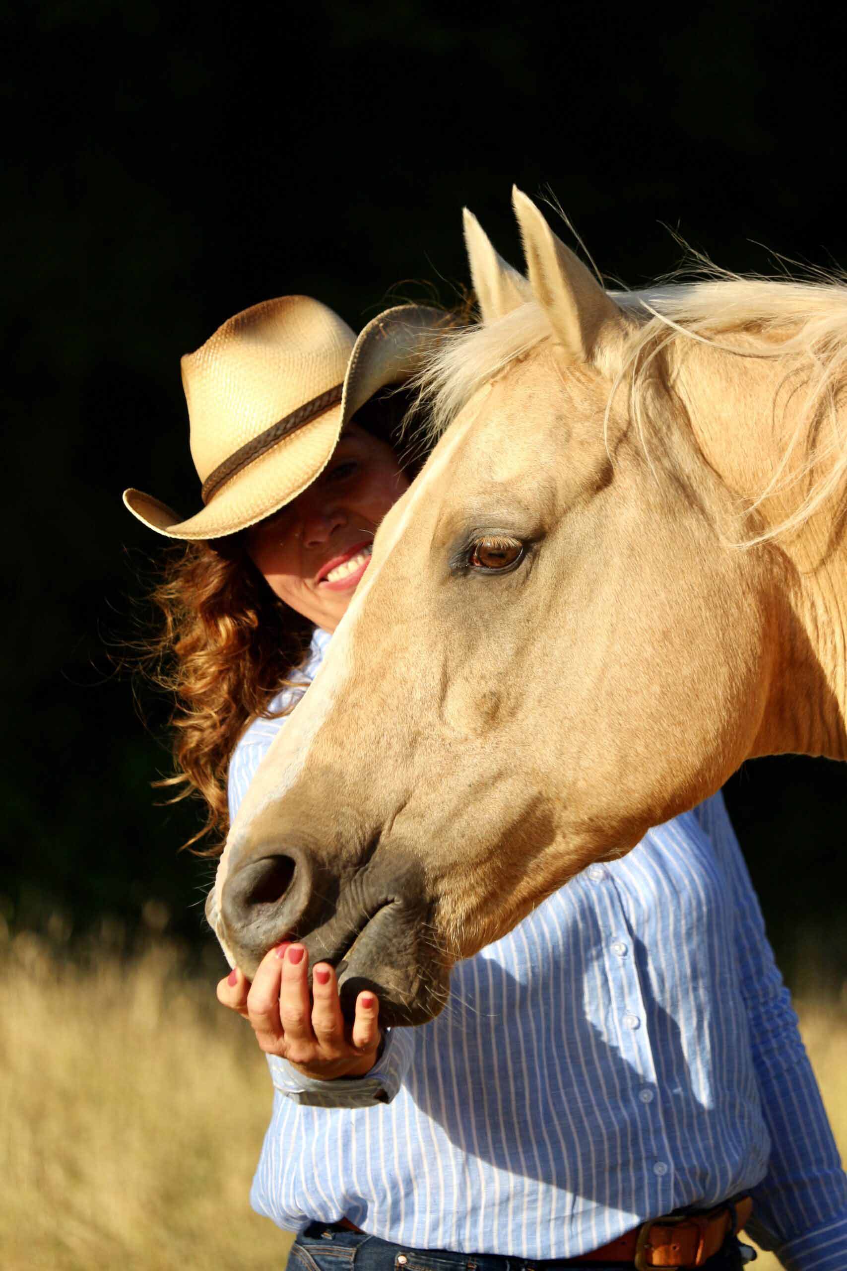 Tierkommunikatorin streichelt ihr Pferd Freeman, trägt einen Cowboyhut und schaut dabei lächelnd in die Kamera.