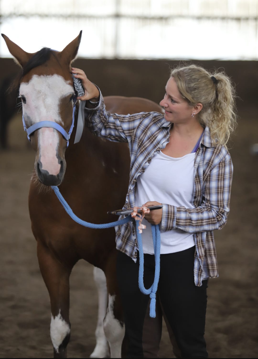 Kundin von Tierkommunikatorin, Nina, schaut ihr Pferd Giorgi in einer Reithalle an